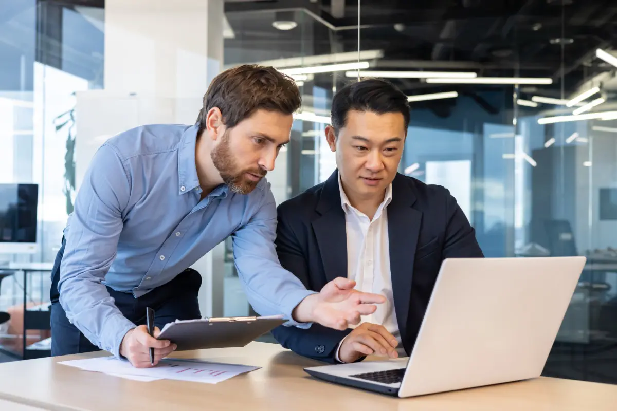 Two businessmen discussing work on laptop.