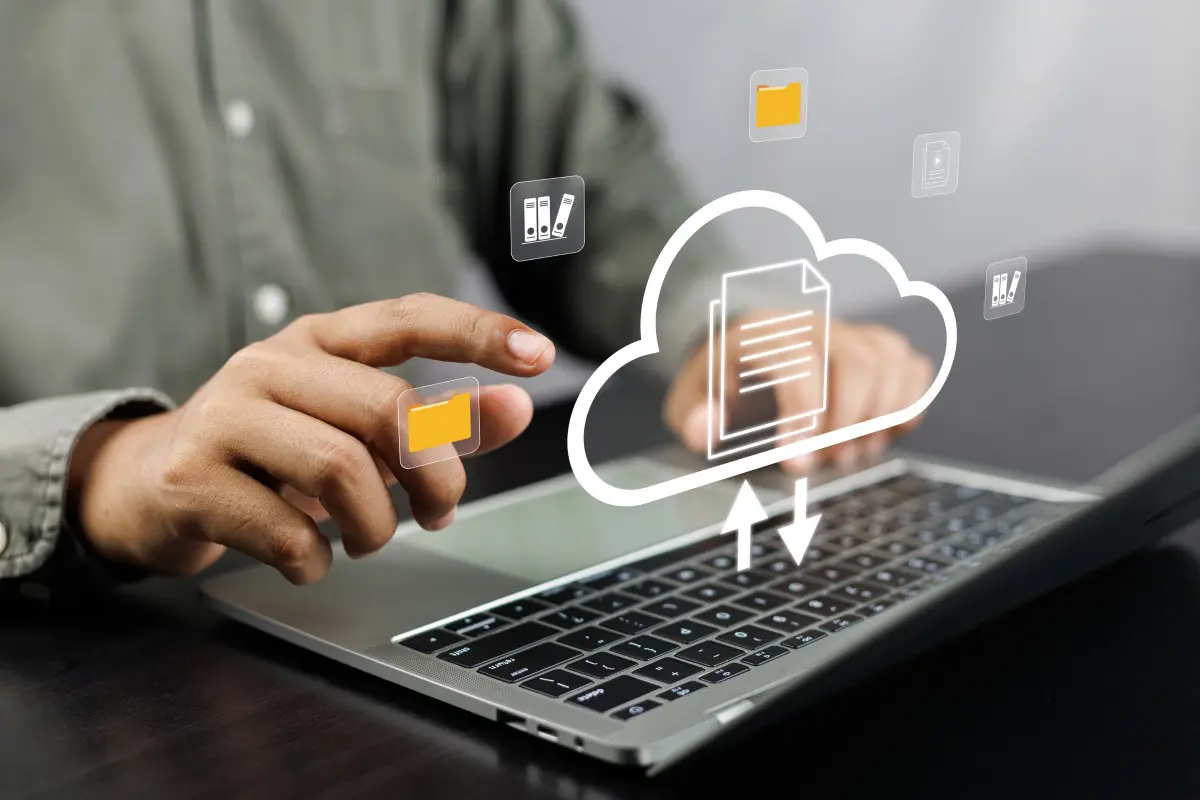 Hands using laptop with cloud computing icons.